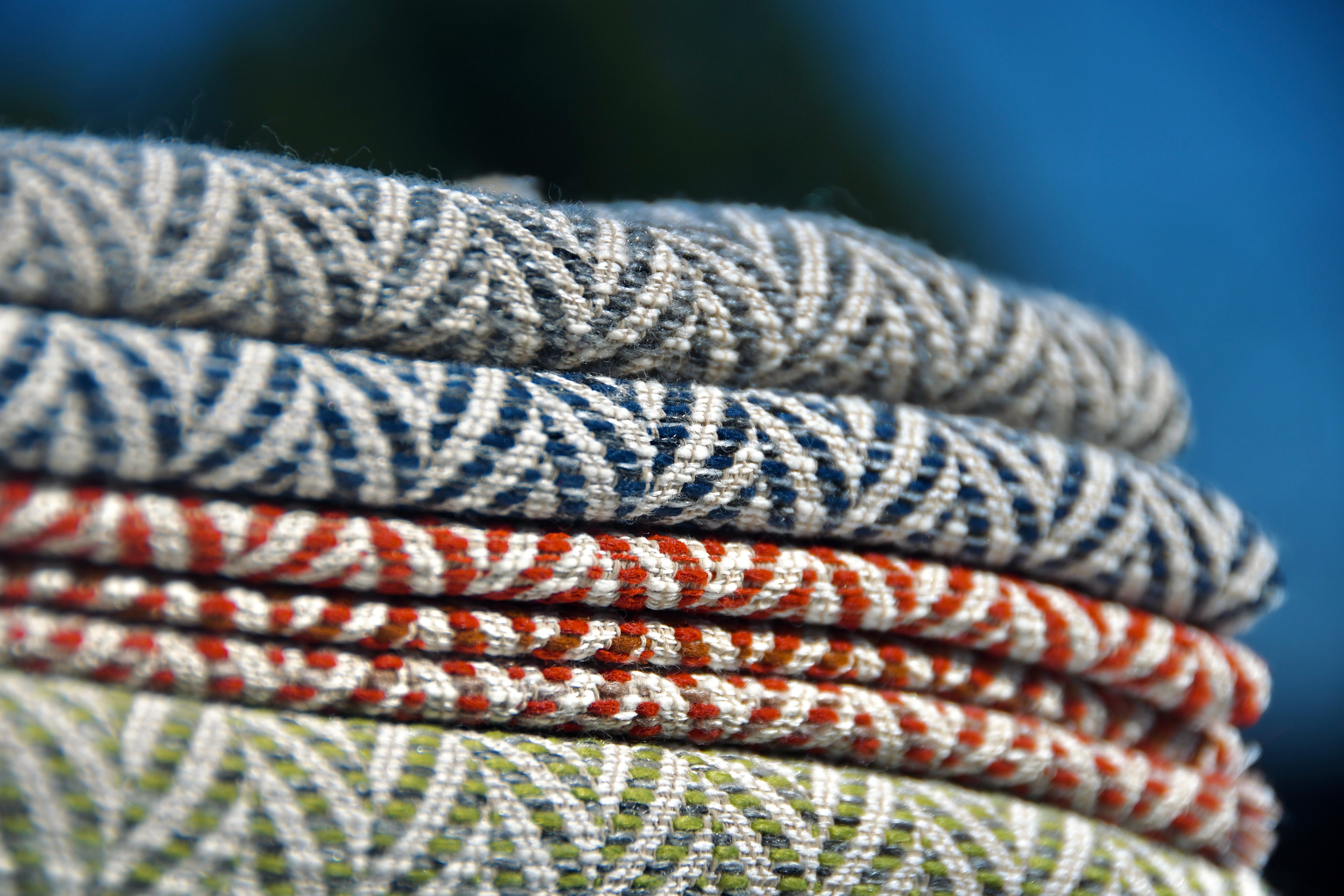 Stacked folded fabrics with colorful woven patterns in grey, blue, red, and green tones.