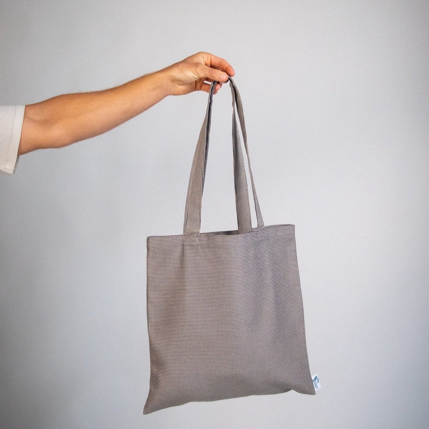Person holding the Agora Navy Tote bag made from water-resistant outdoor fabric with subtle navy stripes – perfect for travel and daily use.