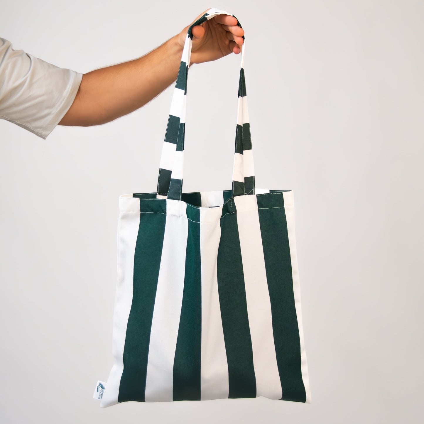 Hand holding a green and white striped Sundowner Tote bag made from durable outdoor fabric.