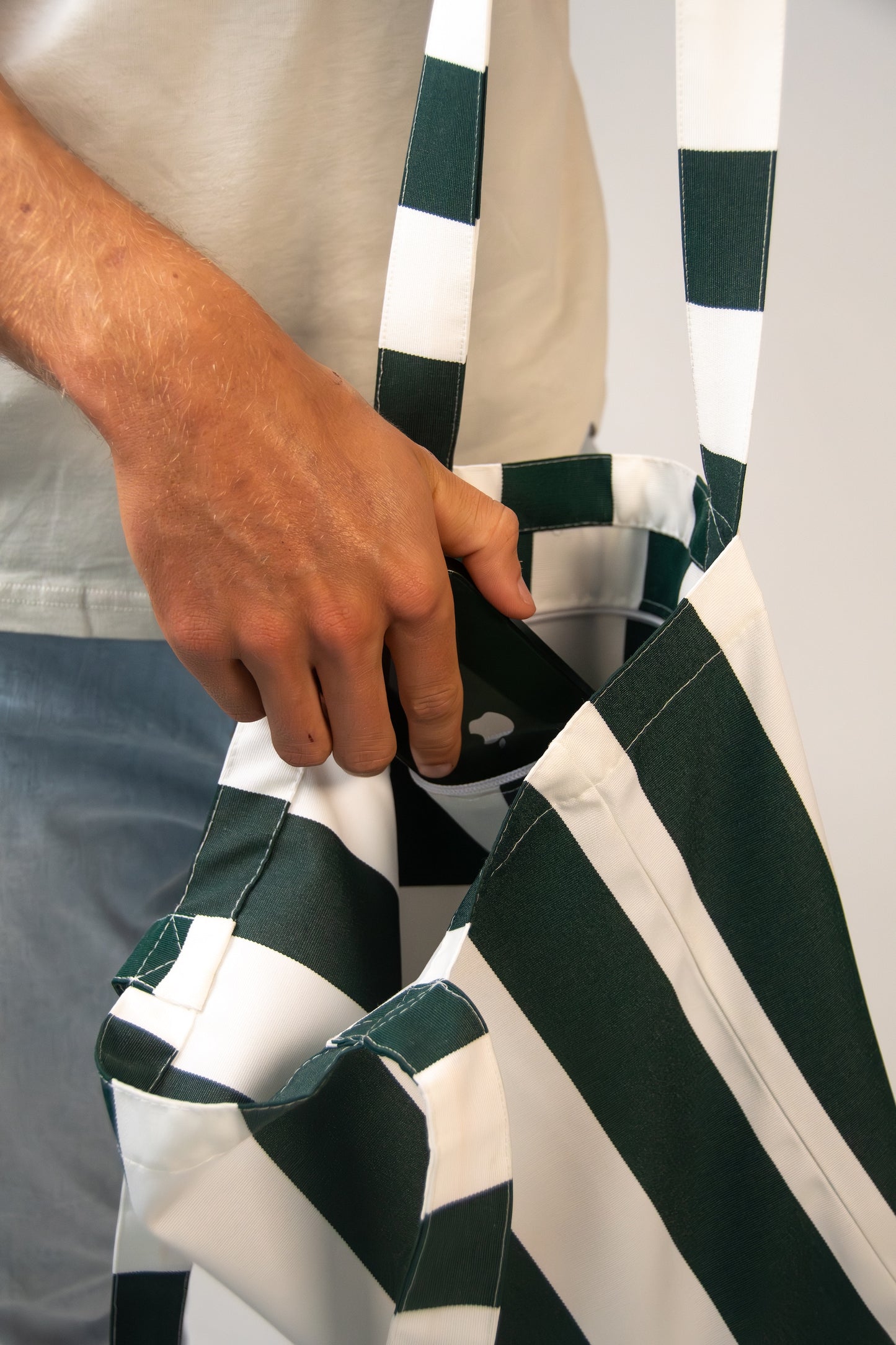 Close-up of a hand placing an item into the Sundowner Tote bag’s secure inner pocket, showcasing striped fabric detail.