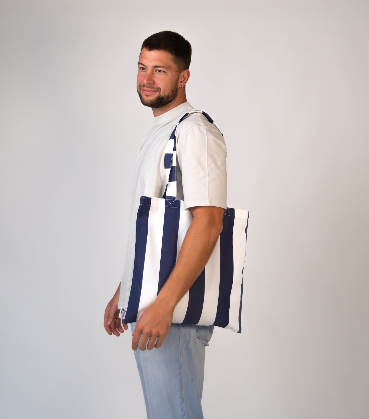 Man wearing Navy striped tote bag over shoulder for scale.