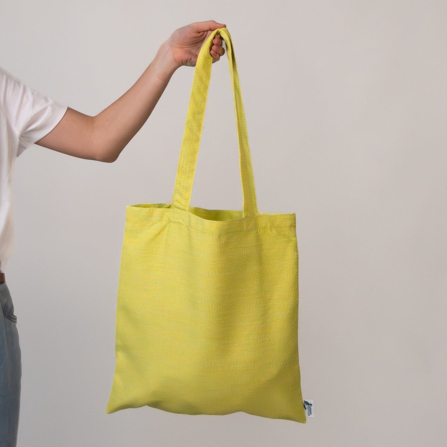 Hand holding the Veranda Chartreuse Tote against a plain background, showcasing its vibrant yellow tone and minimalist design.