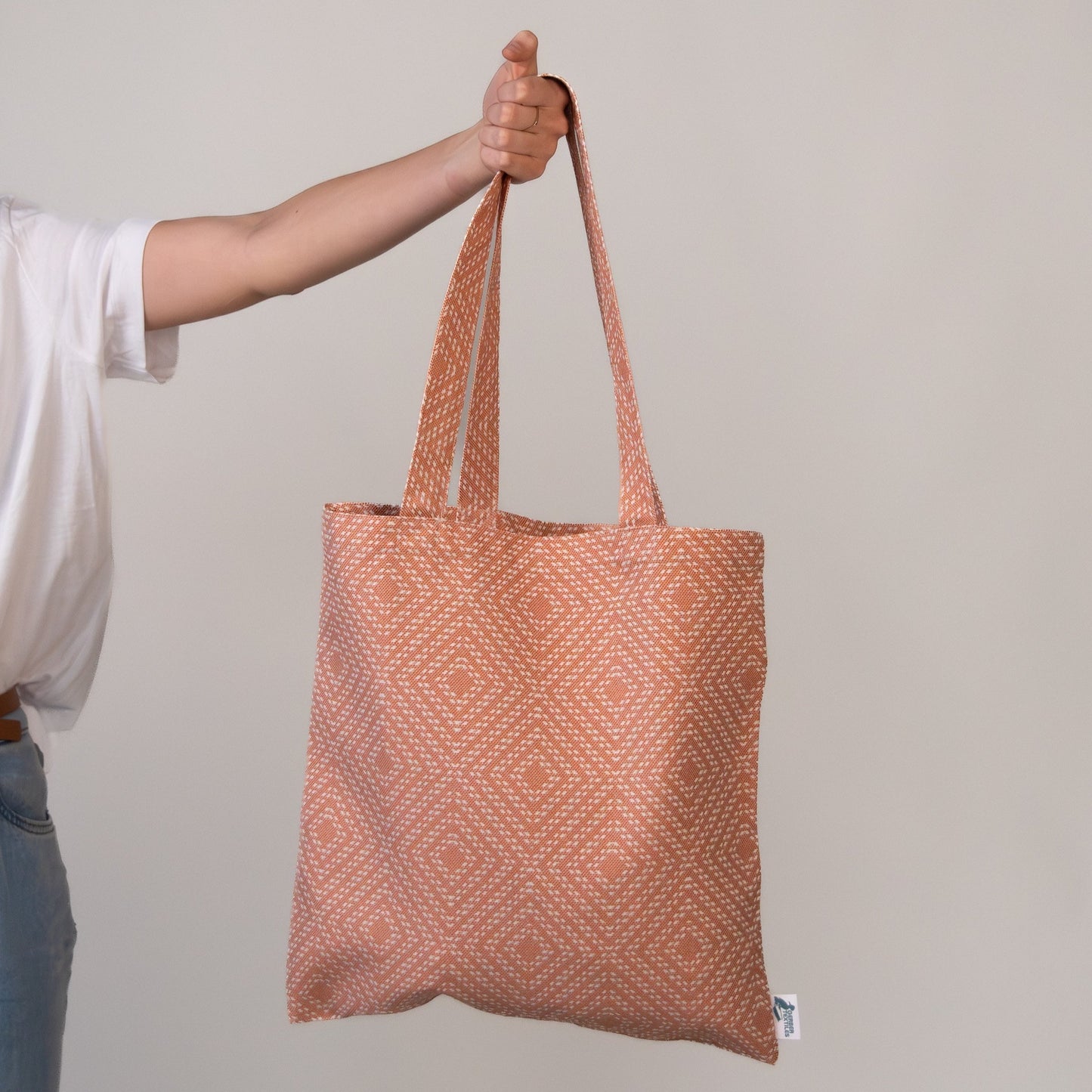 Piazza Sunset Tote Bag with warm orange diamond weave pattern held in hand against neutral background.