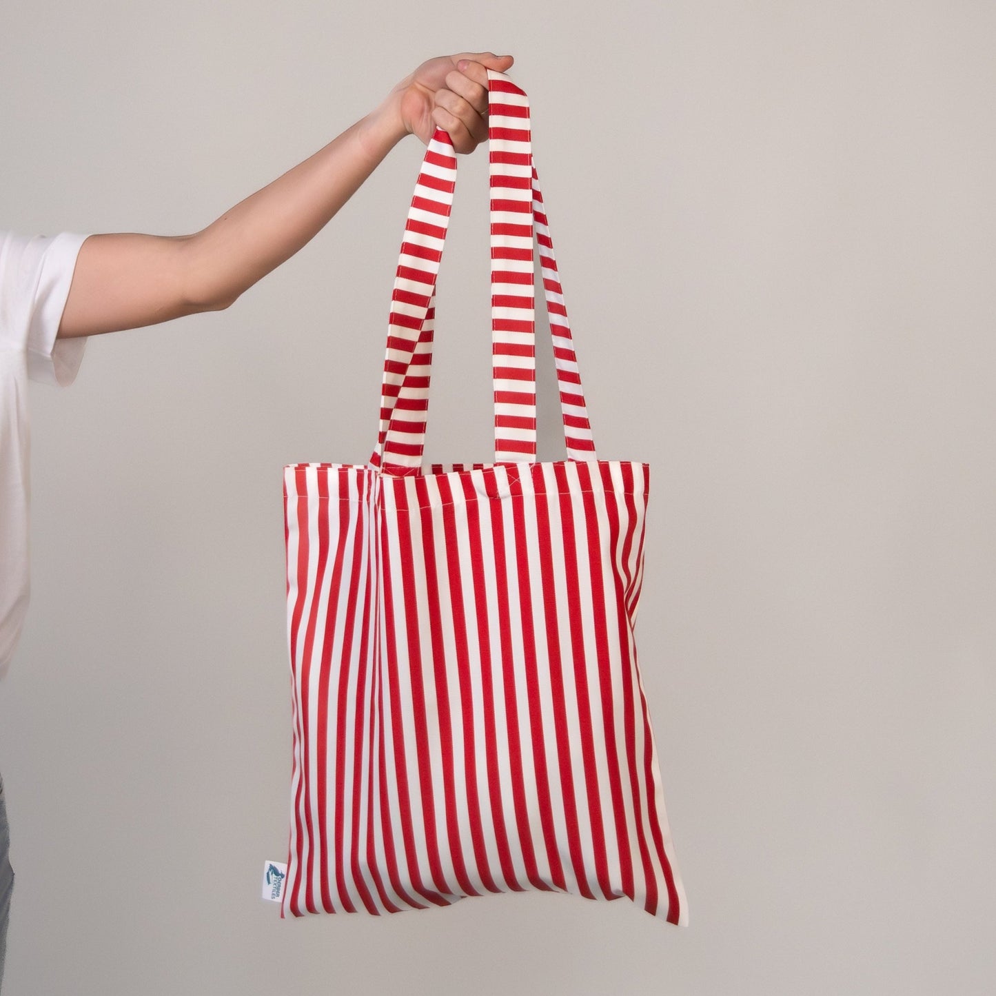 Portofino Red Tote Bag with red and white stripes held by hand – water-resistant outdoor fabric, perfect for travel and beach use.