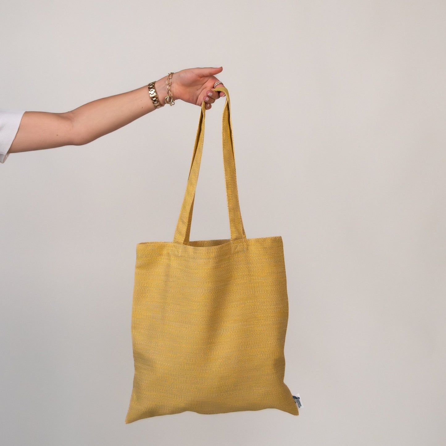 Hand holding the Veranda Mustard Tote made from durable outdoor fabric with UV and water resistance.