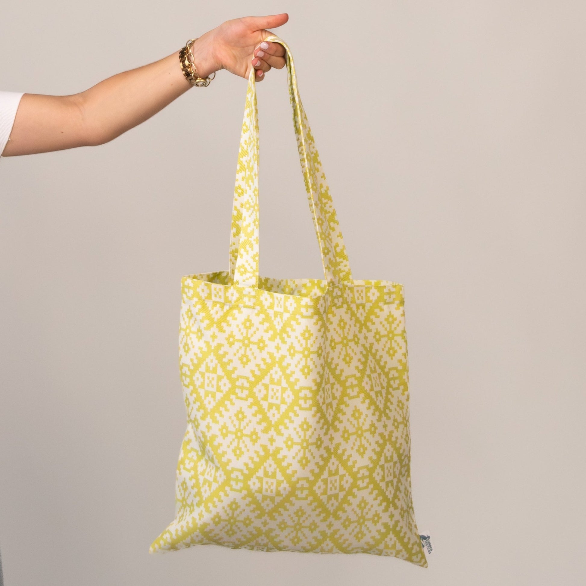 Hand holding Gazebo Chartreuse Tote against neutral background – Stylish yellow patterned tote bag made from water-resistant outdoor fabric.