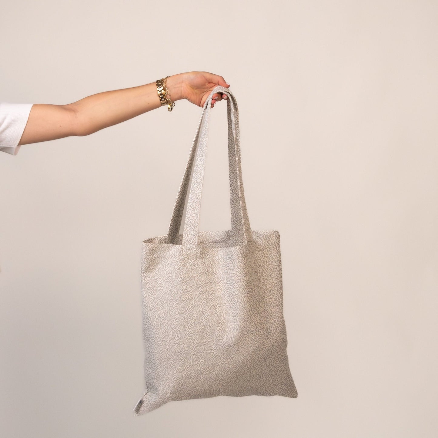 Hand holding light-speckled Picnic Pebbles Tote – neutral-toned and eco-conscious.