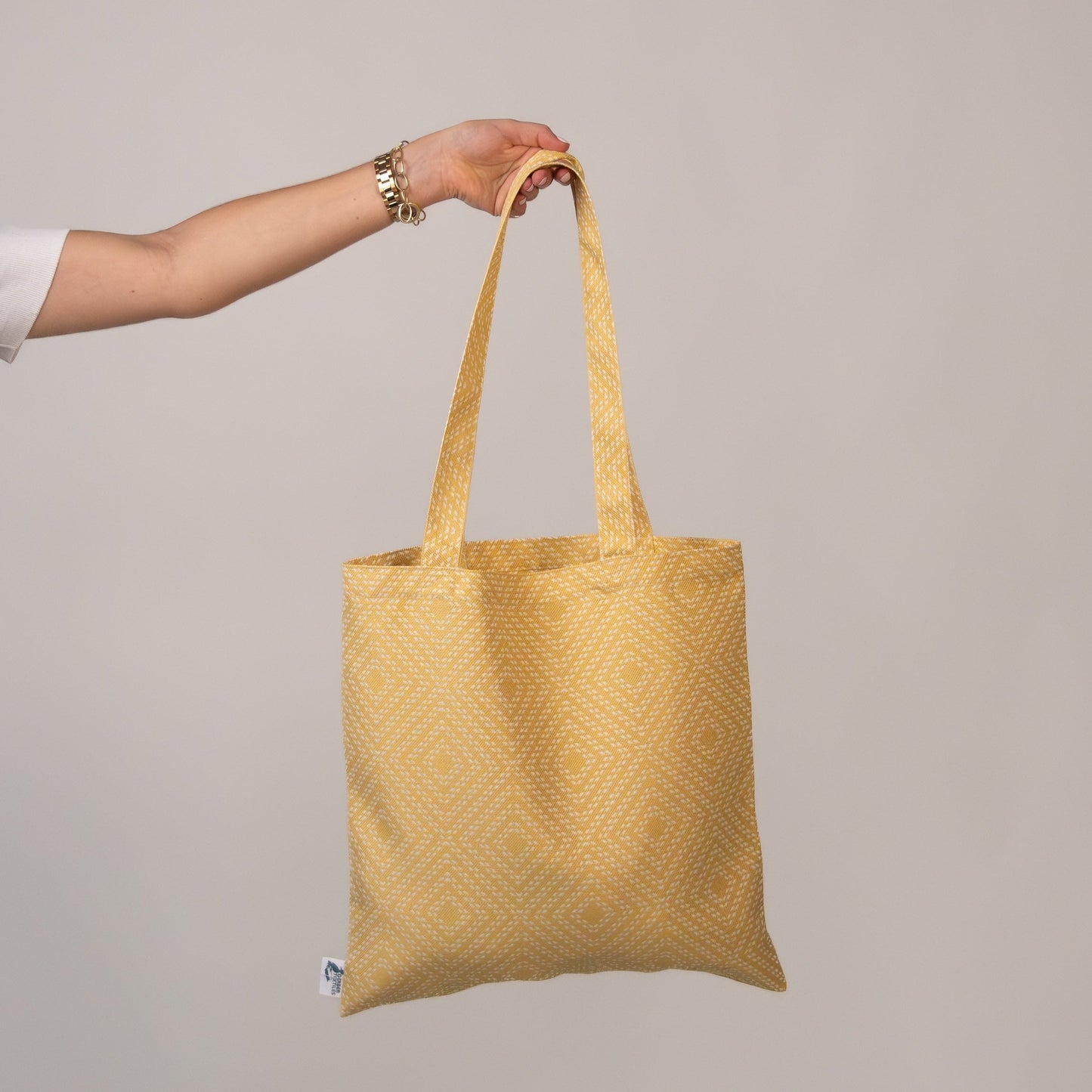 Hand-held view of Piazza Daisy Tote with geometric yellow pattern, crafted from UV and water-resistant outdoor fabric.