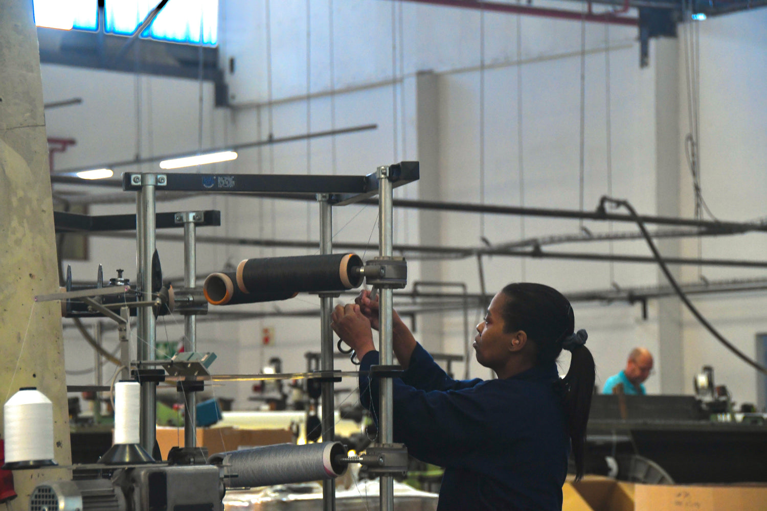 Textile factory worker setting up yarn spools on industrial machinery in a production facility.